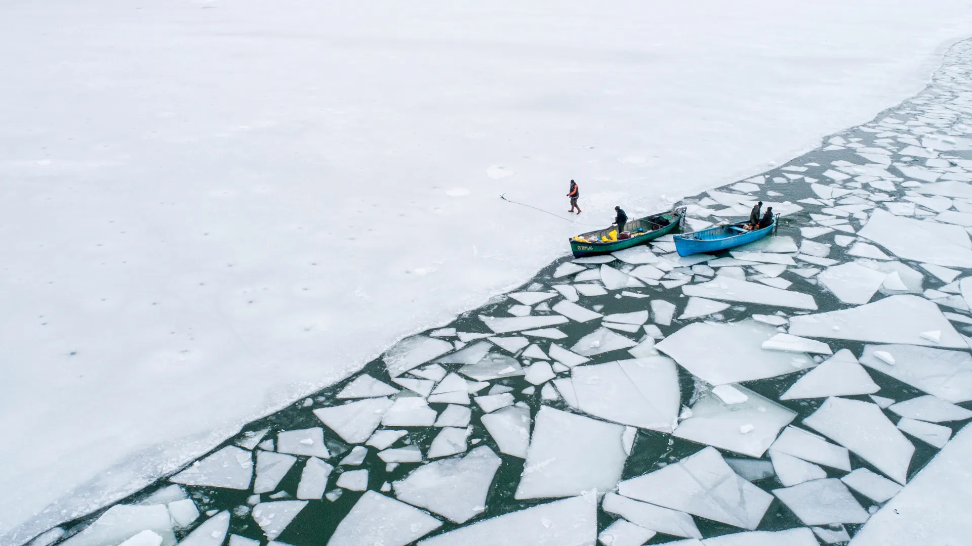 Small boats beside a fractured channel through Arctic sea ice
