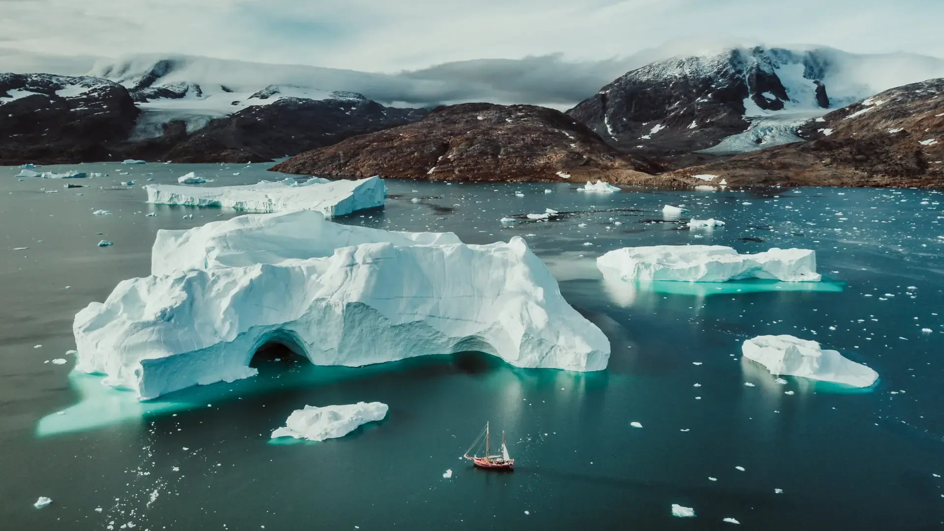 Icebergs scattered across a turquoise fjord beneath snow-dusted mountains