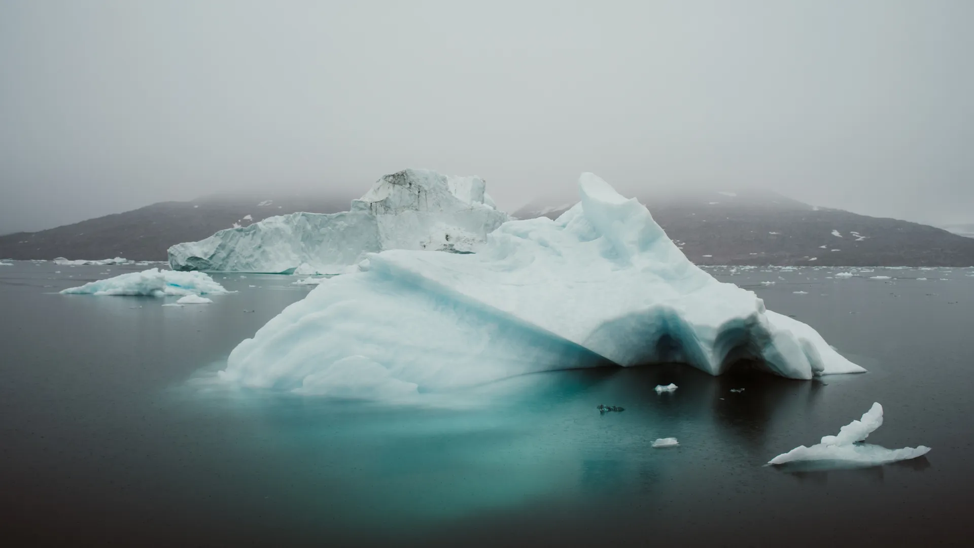 An iceberg floating in still Nordic water beneath a misty sky