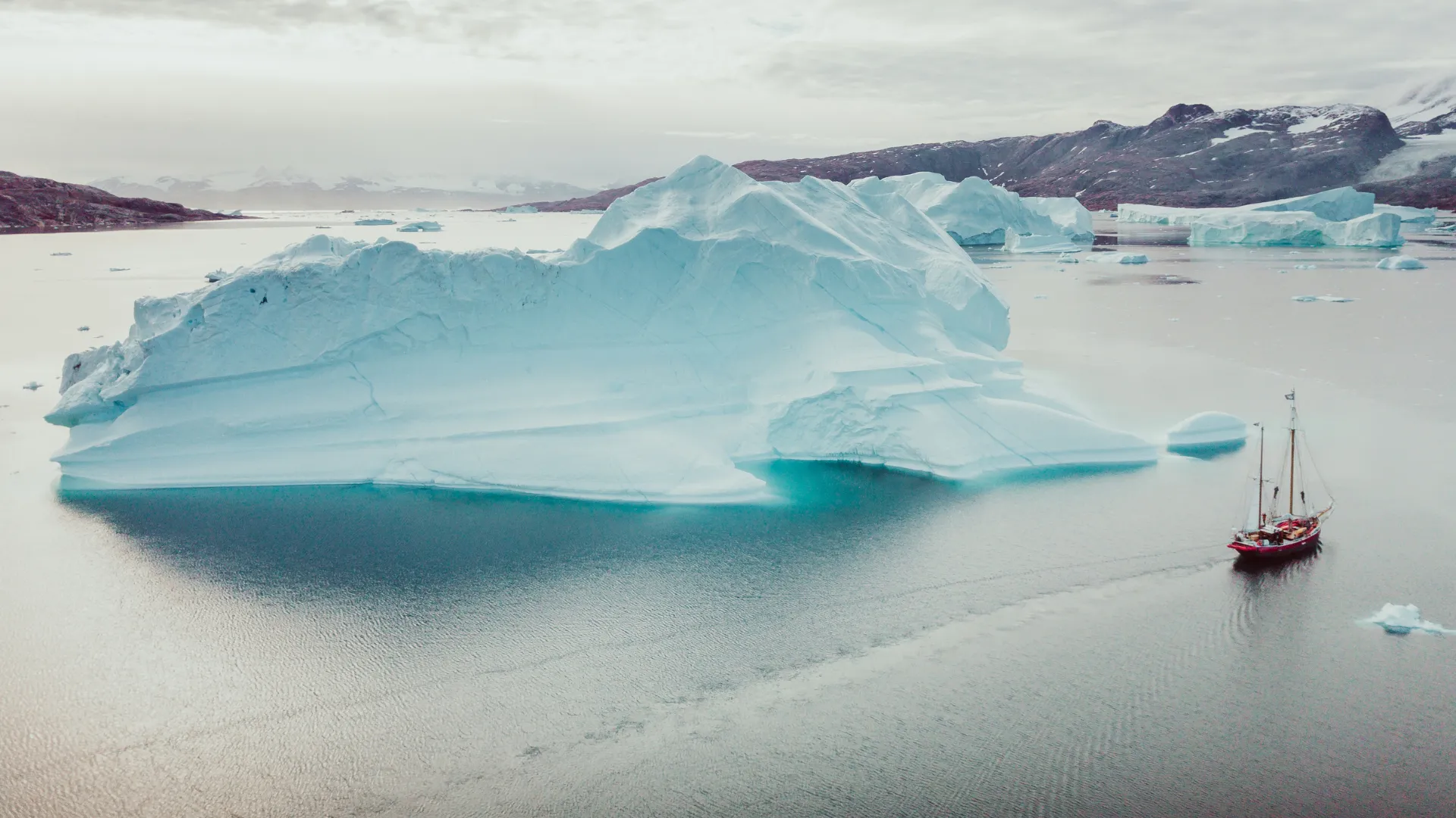 A sailing ship beside a broad turquoise-edged iceberg